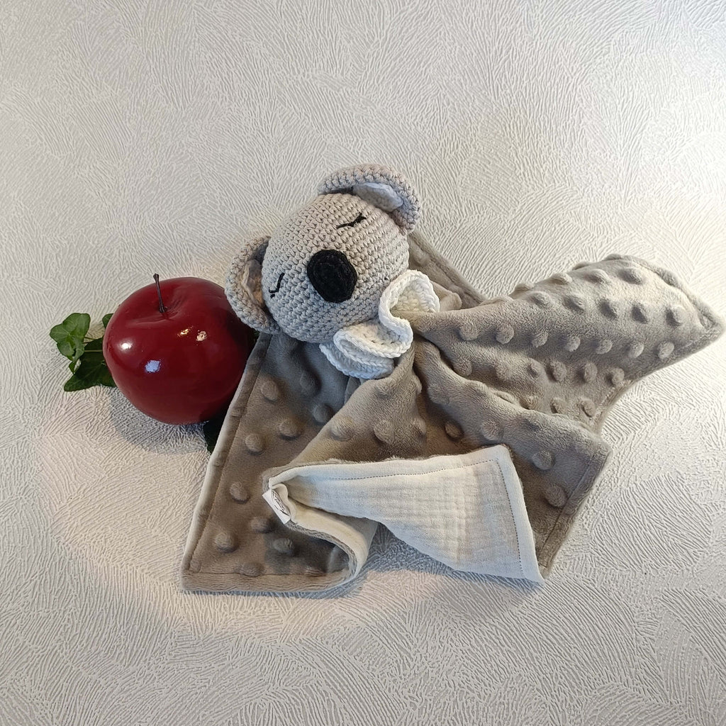 Doudou koala gris en tissu minky avec tête crochetée, à côté d'une pomme rouge