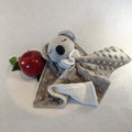 Doudou koala gris en tissu minky avec tête crochetée, à côté d'une pomme rouge