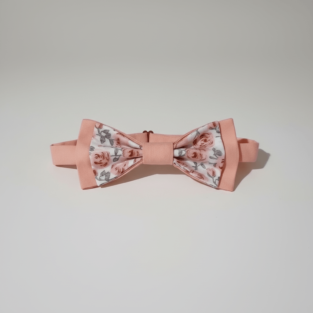 Vue de face d'un nœud papillon pré-noué rose pastel aux motifs de roses anciennes, posé sur fond blanc.