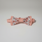 Vue de face d'un nœud papillon pré-noué rose pastel aux motifs de roses anciennes, posé sur fond blanc.