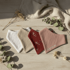 Lot de quatre bandanas bébé en coton, couleurs naturelles et motif floral, personnalisable, posé sur bois clair.