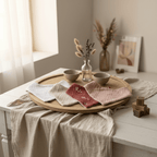 Lot de quatre bavoirs bandana bébé en double gaze brodée, coloris blanc ivoire beige terracotta et rose poudré, disposés en éventail sur plateau en bois avec fleurs séchées