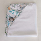 Cape de bain bébé personnalisable pliée vue de dessus, bordure motif éléphant et animaux safari aquarelle tons bleus et verts, éponge blanche, faite main L'Atelier de Megh