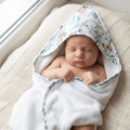 Nouveau-né endormi enveloppé dans la cape de bain personnalisée motif éléphant safari et eucalyptus, fond tricoté ivoire