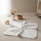 Sortie de bain bébé blanche à motifs, posée sur tapis dans une chambre enfant, ambiance douce.