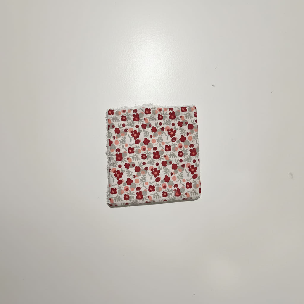Gros plan sur une lingette lavable carrée en coton à motif petites fleurs rouges.