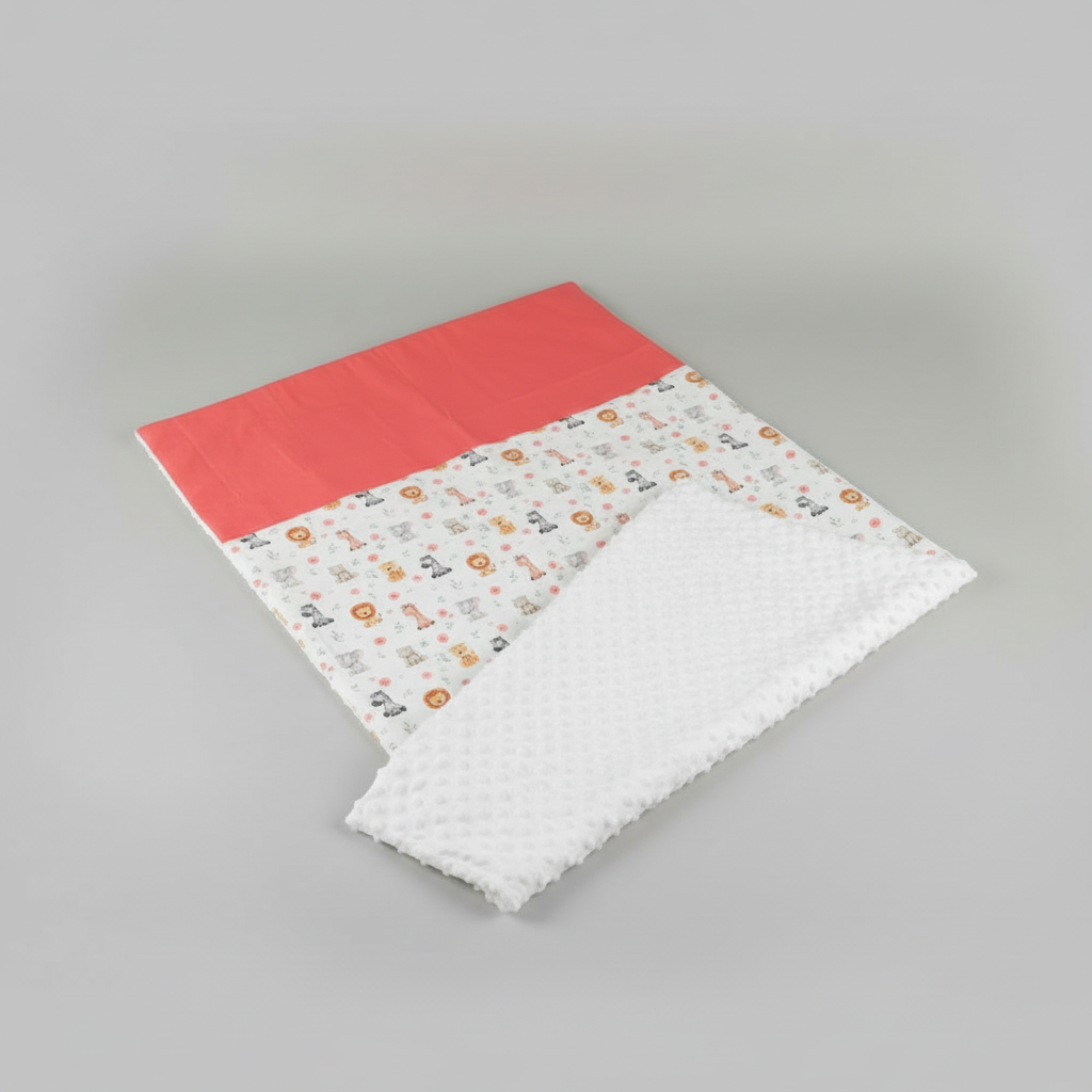 Couverture pour bébé bi-matière : face en coton motif animaux de la savane et bande corail, doublée en tissu minky à pois blanc ultra-doux.