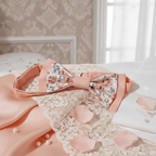 Gros plan sur un nœud papillon rose à fleurs posé délicatement sur de la dentelle blanche et des pétales de roses.