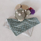 Vue du dessus du doudou dinosaure au crochet vert sauge, lange double face minky vert sauge à bulles et mousseline blanche