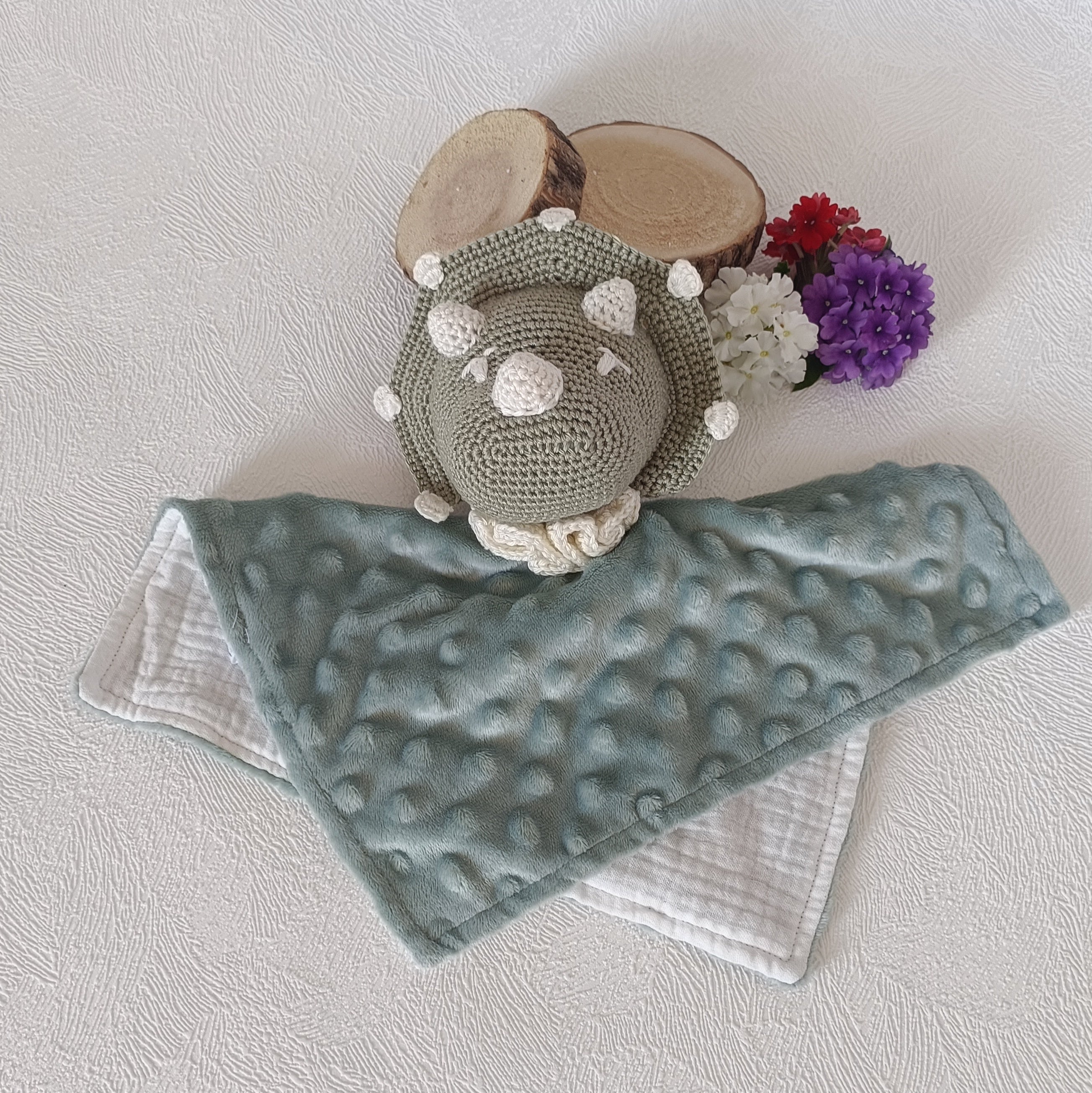 Vue du dessus du doudou dinosaure au crochet vert sauge, lange double face minky vert sauge à bulles et mousseline blanche