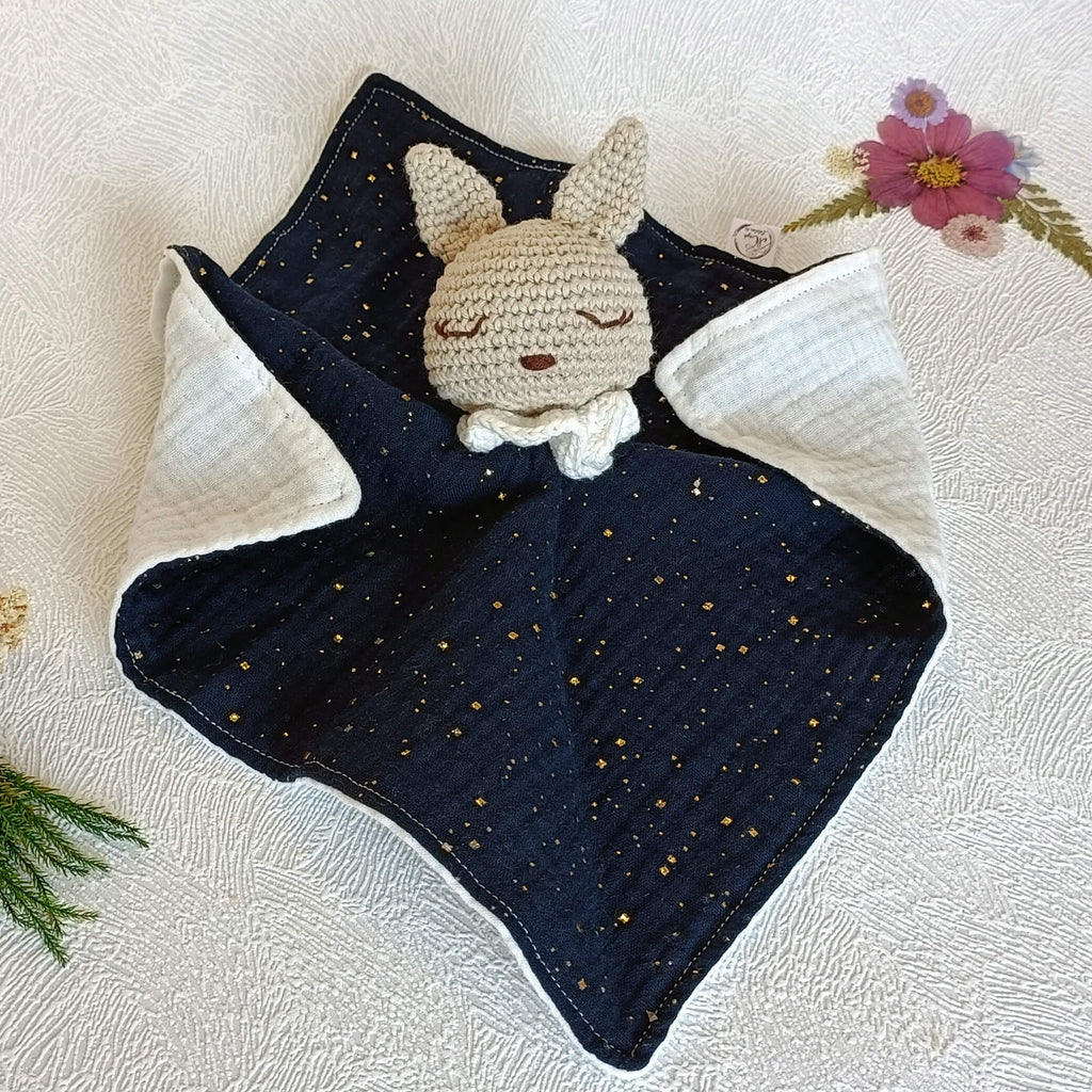 Doudou plat lapin au crochet, corps en double gaze de coton bleu marine parsemé de pois dorés brillants.