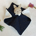 Doudou plat lapin au crochet, corps en double gaze de coton bleu marine parsemé de pois dorés brillants.