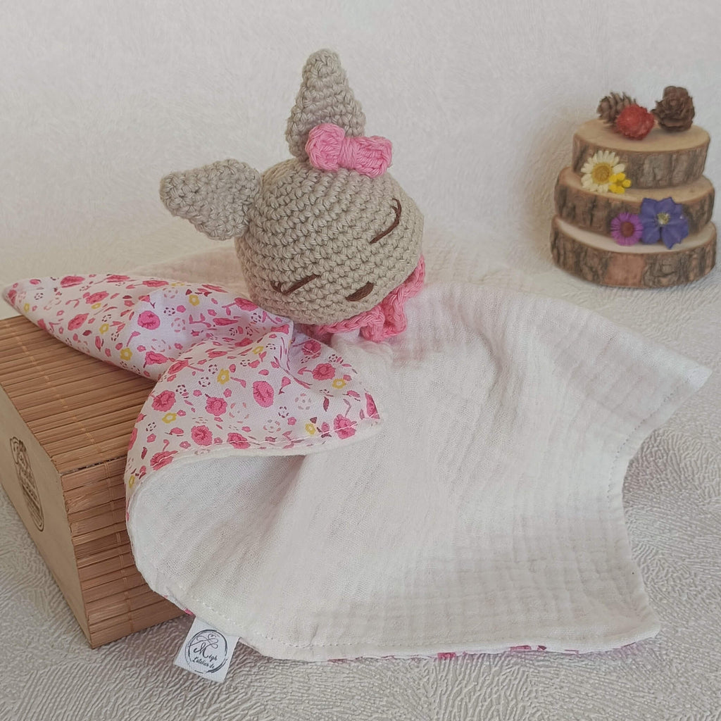 Doudou lapin au crochet avec petit nœud rose, corps en gaze de coton blanche et revers à motifs petites fleurs roses.