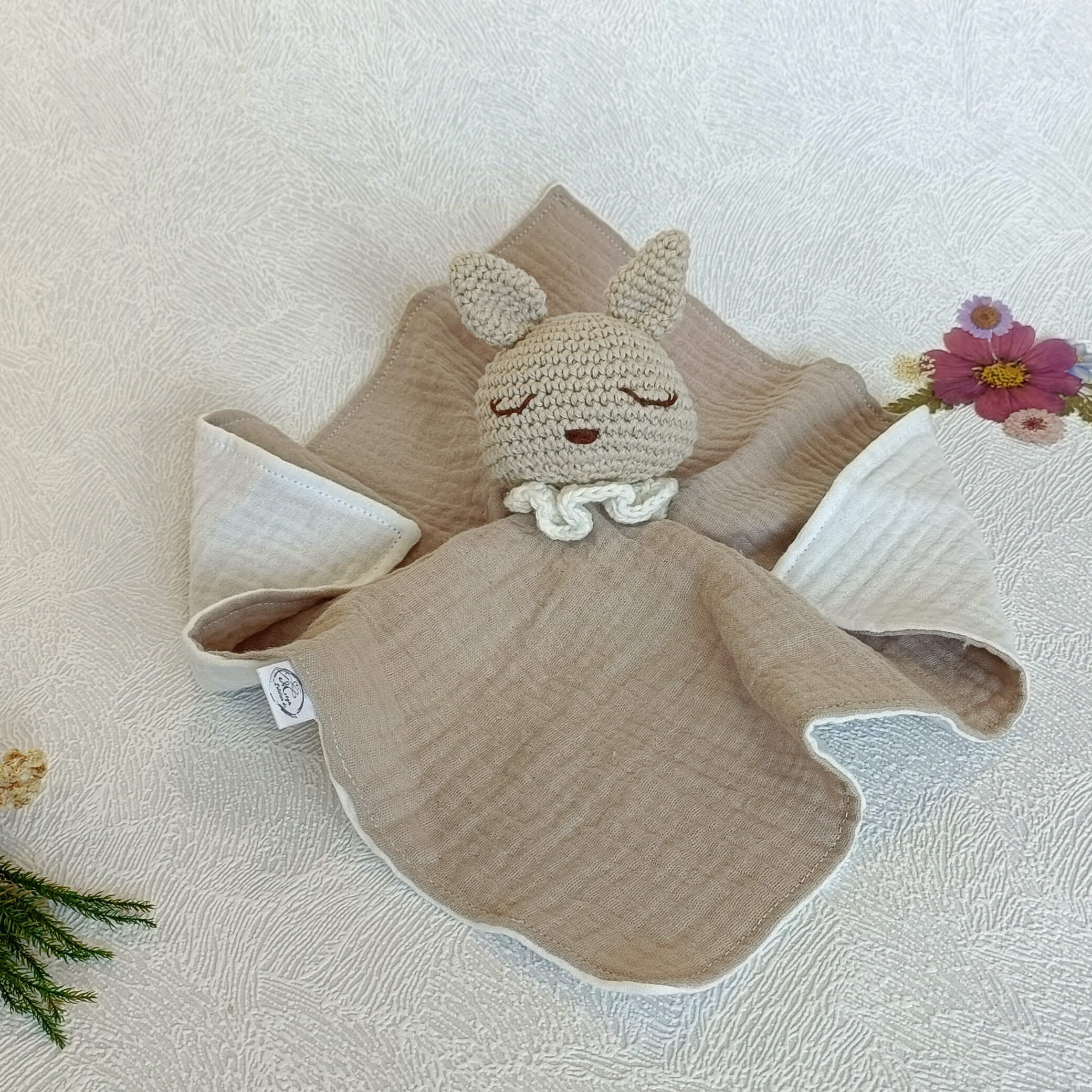 Vue à plat d'un doudou lapin artisanal beige en coton, idéal comme cadeau de naissance mixte.
