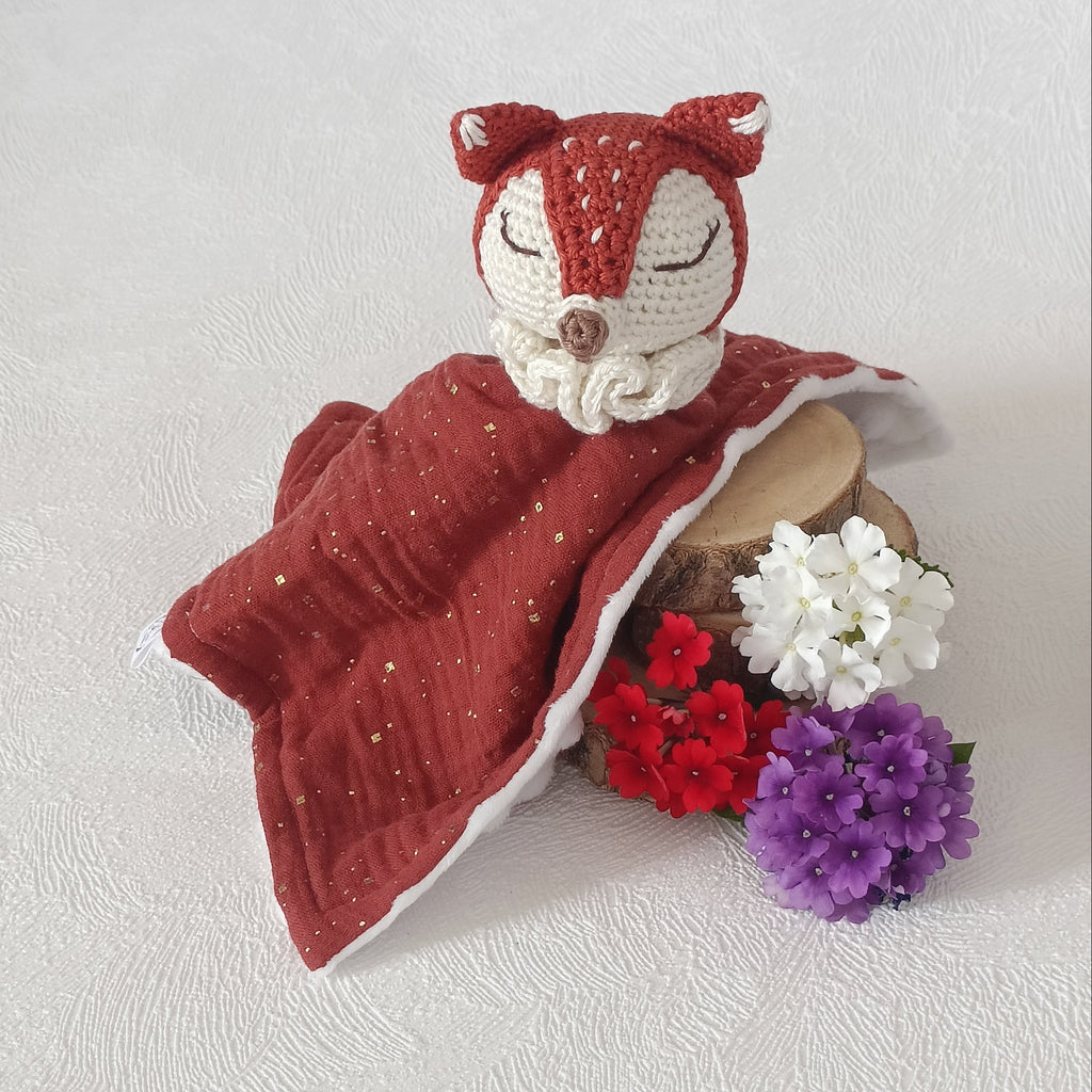 Gros plan du doudou renard au crochet terracotta et blanc, lange mousseline bordeaux à micro-paillettes dorées doublé minky blanc
