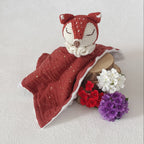 Gros plan du doudou renard au crochet terracotta et blanc, lange mousseline bordeaux à micro-paillettes dorées doublé minky blanc