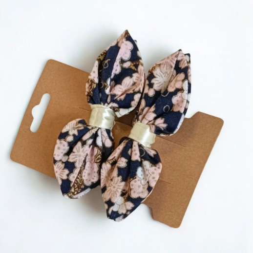 Duo de barrettes à cheveux forme nœud en tissu japonais fond bleu marine avec motif fleurs de cerisier roses pâles. Centre du nœud en ruban satiné crème.