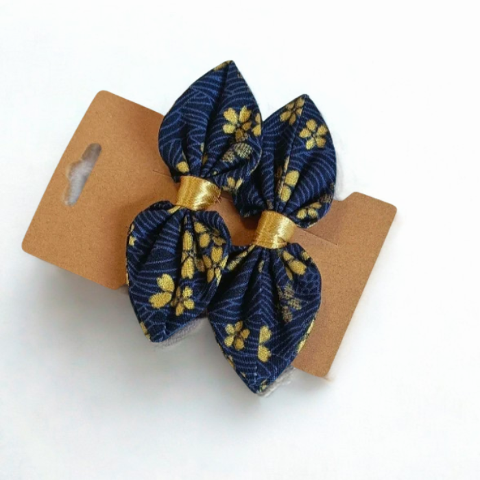 Duo de barrettes à cheveux forme nœud en tissu japonais bleu marine parsemé de petites fleurs dorées. Centre du nœud en ruban or.