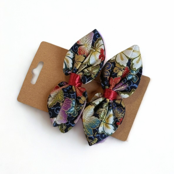 Duo de barrettes à cheveux forme nœud en tissu japonais fond bleu sombre avec motif floral riche et multicolore (blanc, rouge, violet, or). Centre du nœud en ruban satiné rouge.