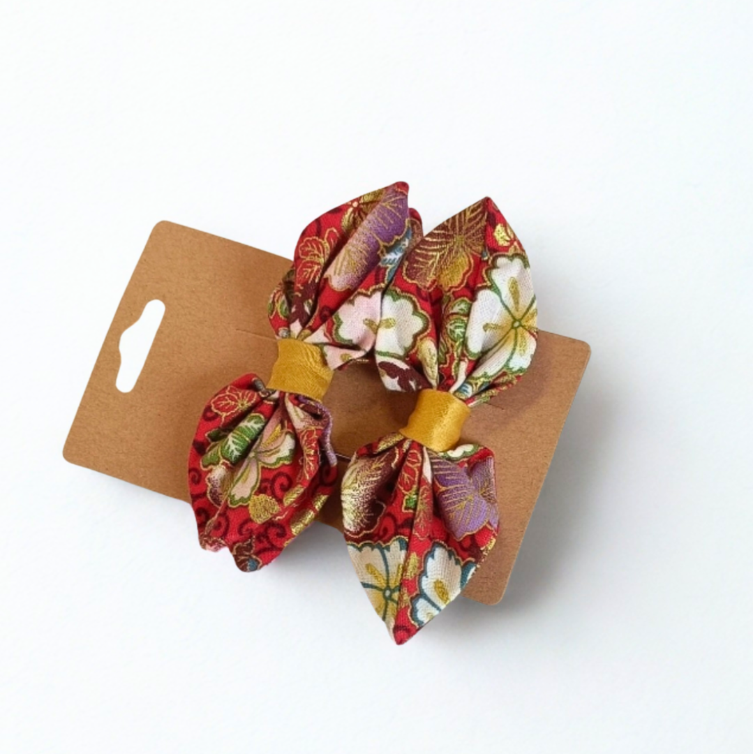 Duo de barrettes à cheveux forme nœud en tissu japonais fond rouge avec motifs floraux dorés, blancs et violets. Centre du nœud en ruban doré.