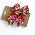 Duo de barrettes à cheveux forme nœud en tissu japonais rouge vif avec motif fleurs de cerisier (Sakura) roses et touches vertes. Centre du nœud en ruban rouge satiné.