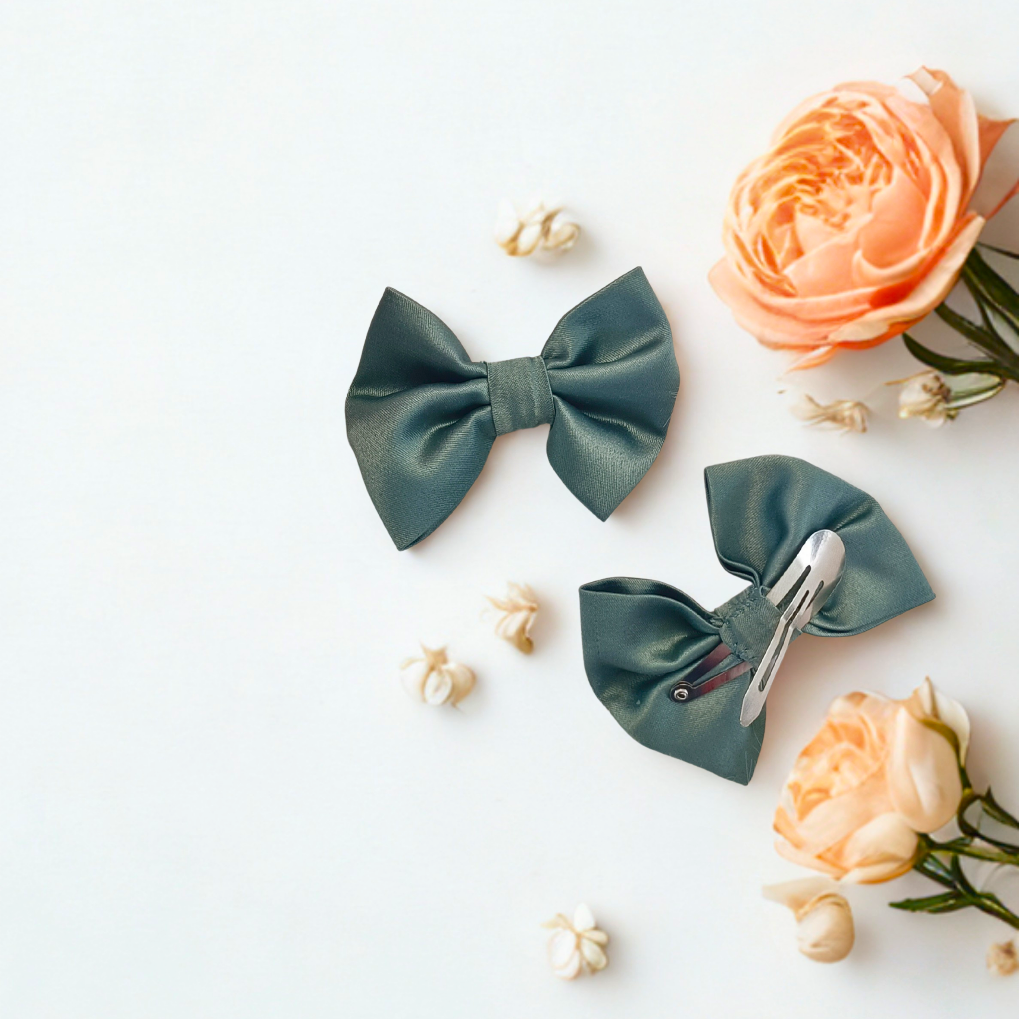 Duo de barrettes à cheveux forme nœud en satin vert sauge. Vue recto et verso montrant l'attache clic-clac métallique adaptée aux enfants. Décoration florale mariage.