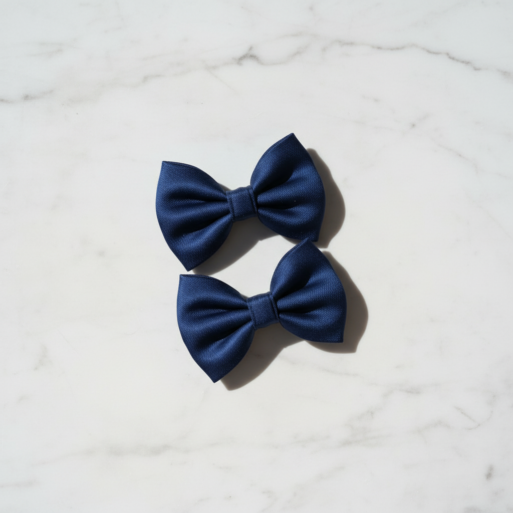 Vue de dessus de deux barrettes nœuds papillon bleu marine en tissu posées sur une surface en marbre blanc.