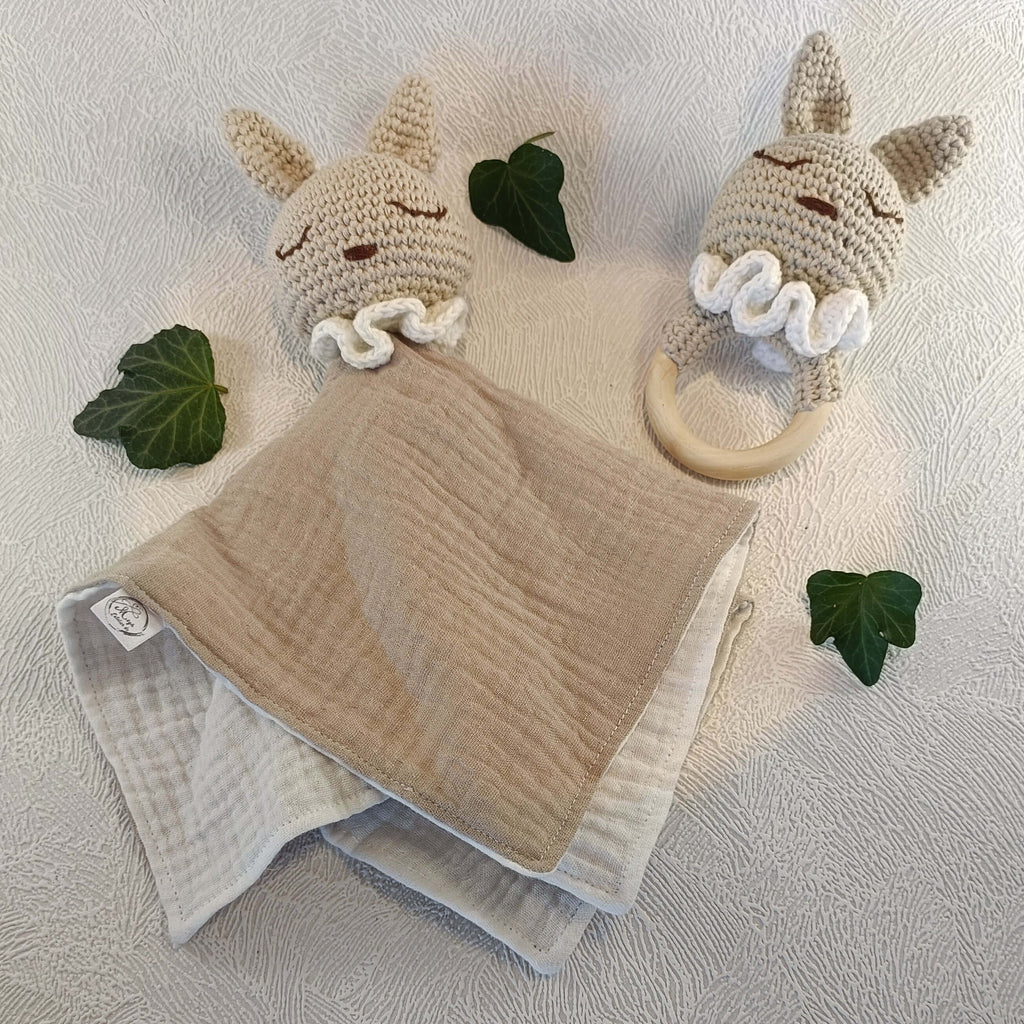 Doudou lapin en coton beige et hochet bébé au crochet, décorés de feuilles sur fond clair.