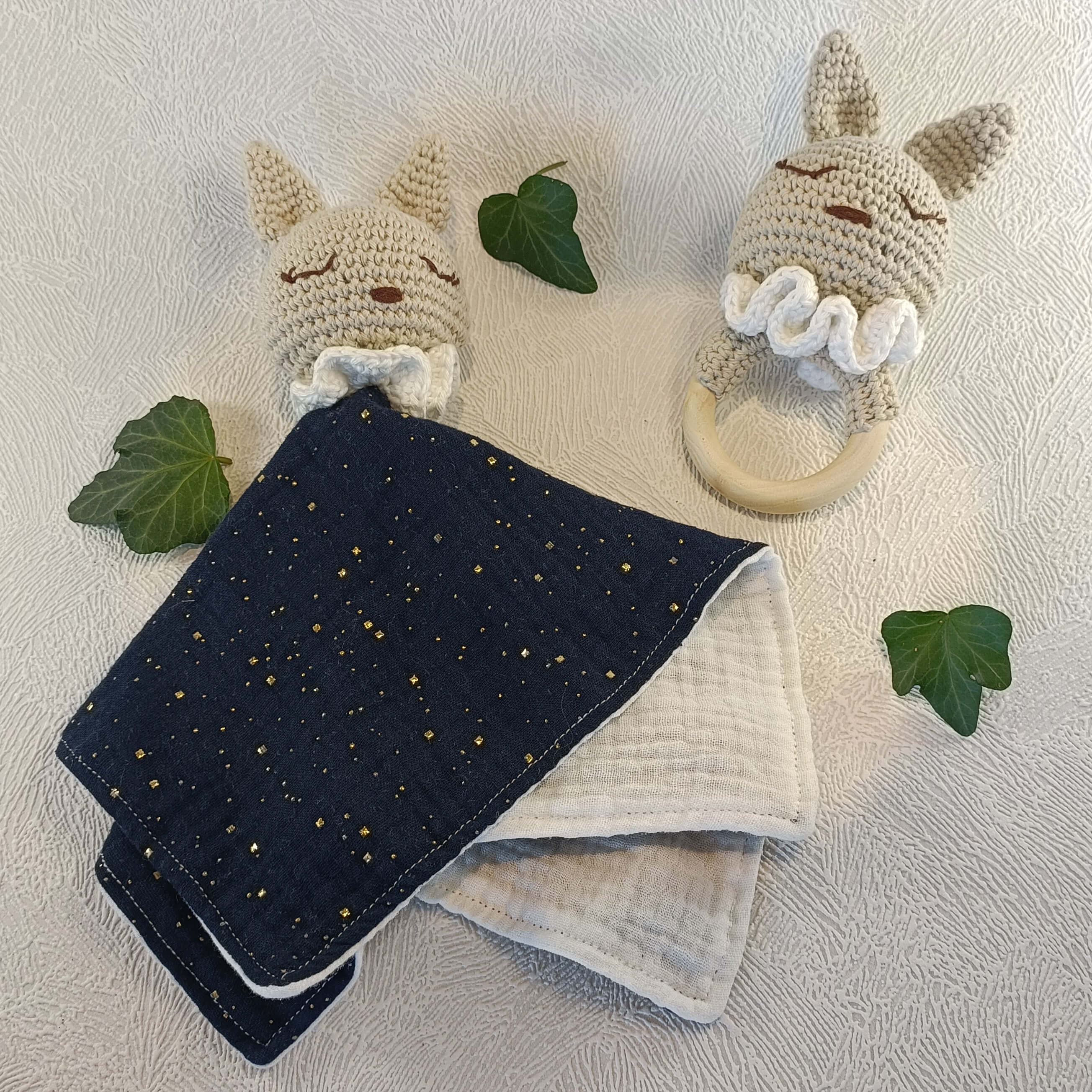 Doudou lapin crocheté avec anneau de dentition en bois et lapin crocheté sur fond clair décoré de feuilles.