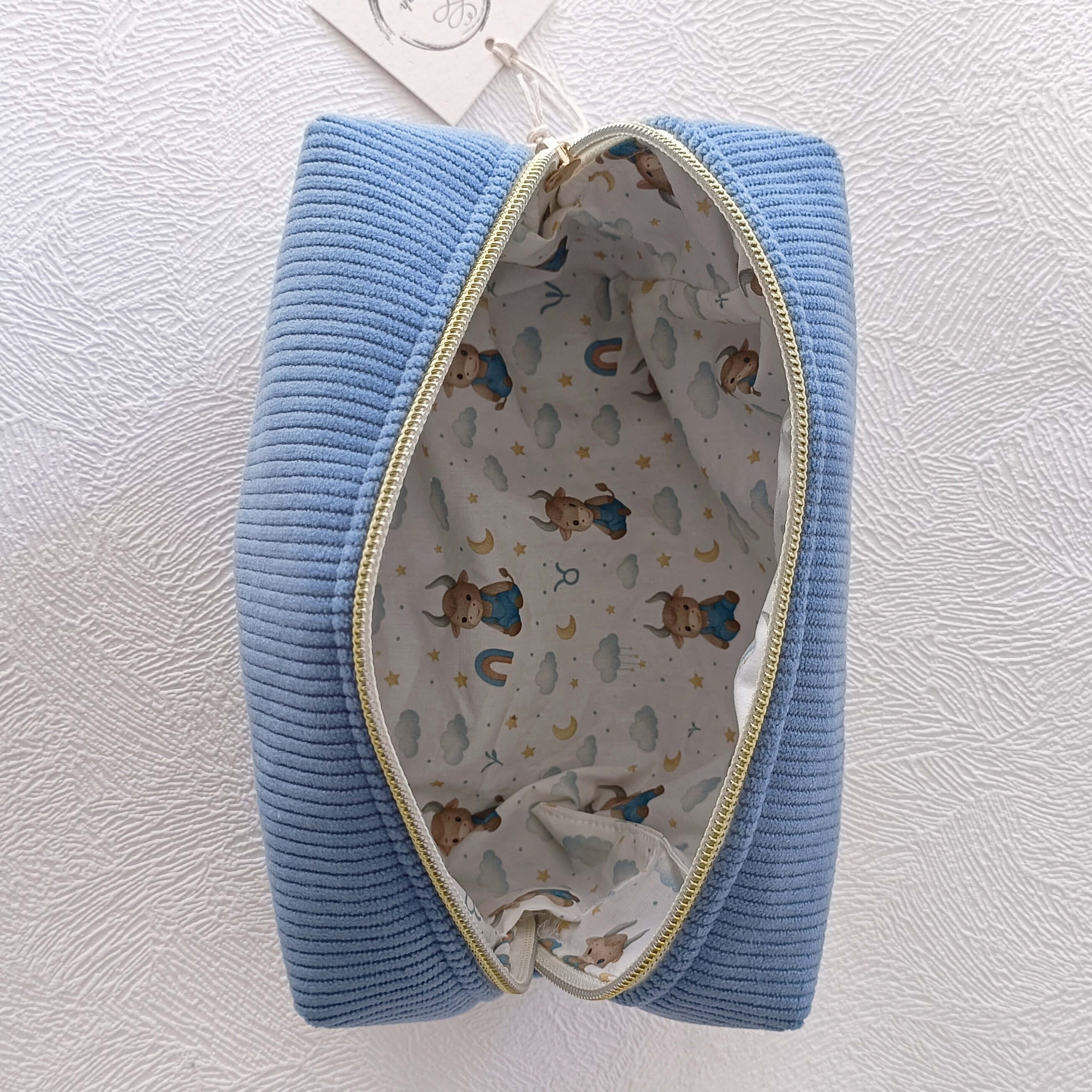 Vue de dessus de la grande trousse artisanale en velours côtelé bleu ouverte — doublure motif taureau zodiac aquarelle étoiles et nuages, fermeture éclair dorée, faite main