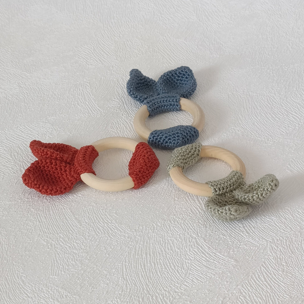 Vue du dessus des trois hochets anneaux en bois avec nœud au crochet terracotta, bleu ardoise et vert sauge
