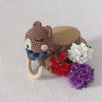 Hochet anneau en bois naturel avec ours au crochet marron et col bleu, vue de profil