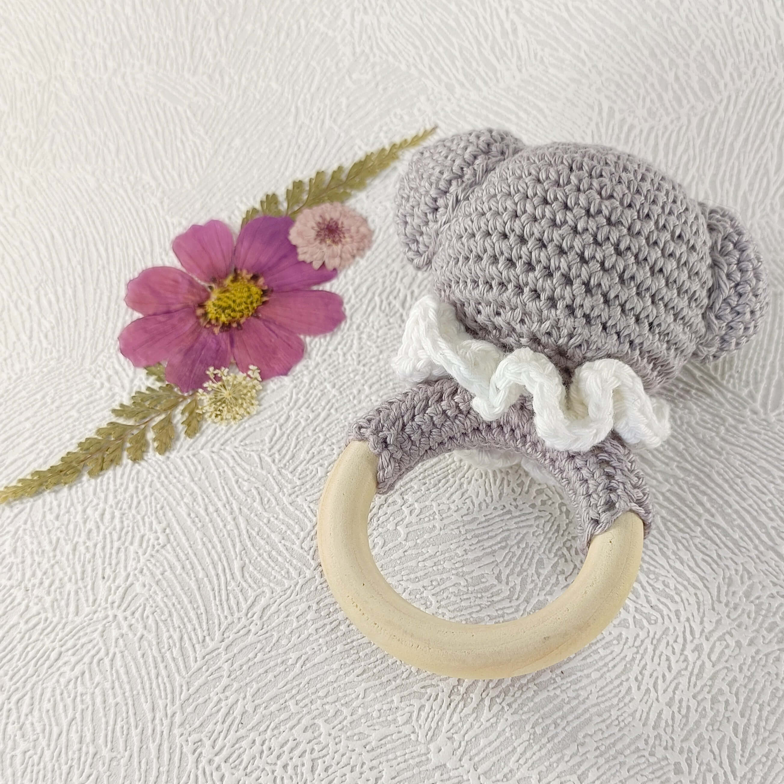 Hochet bébé au crochet en forme koala gris avec anneau bois, sur fond fleuri élégant