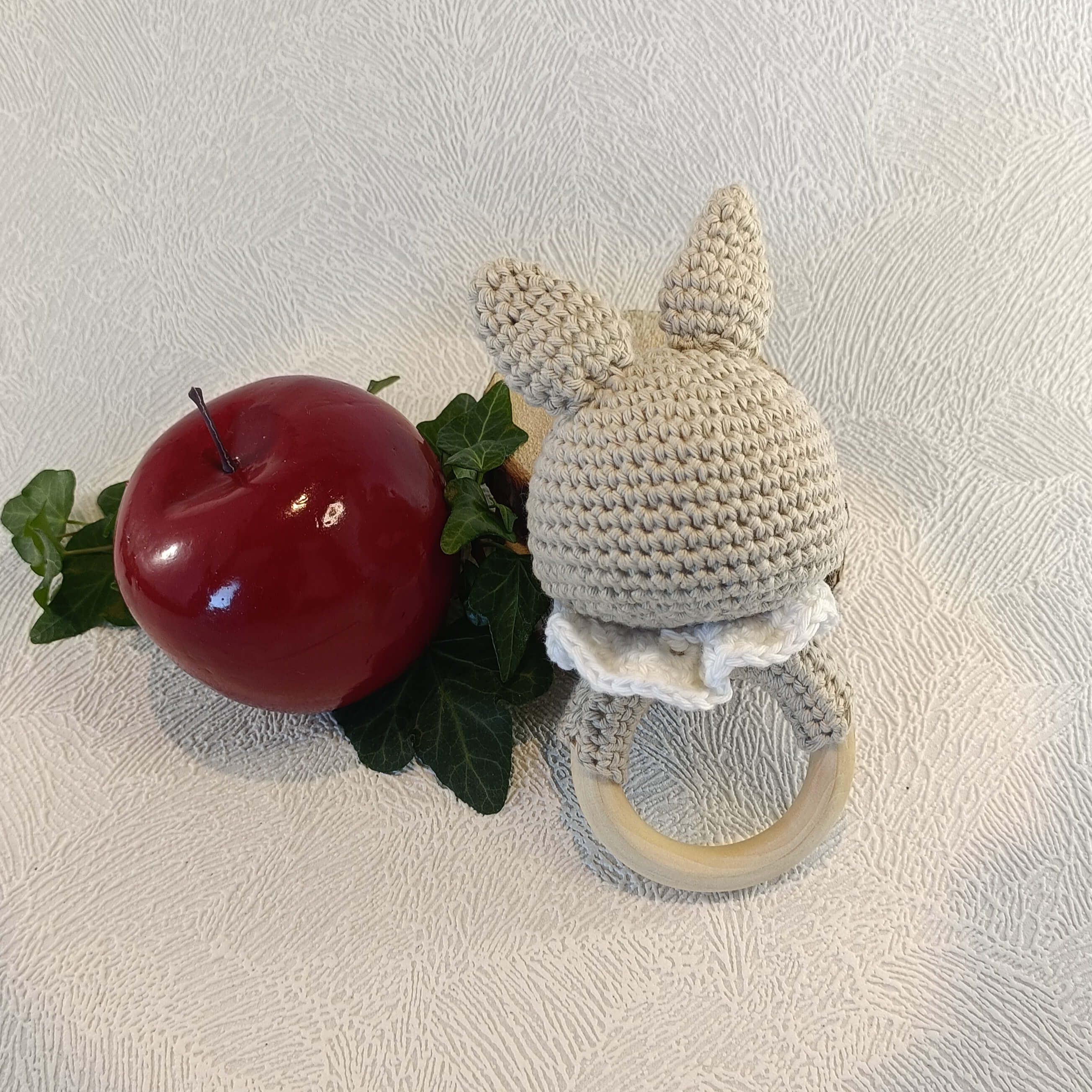 Hochet en crochet lapin avec oreilles, collerette blanche, pomme rouge et feuilles vertes.