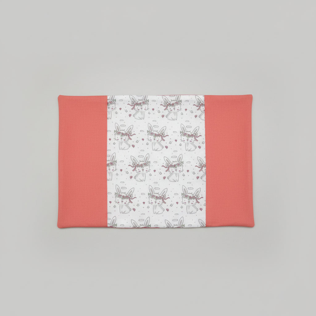 Vue dépliée d'un protège carnet de santé montrant le tissu central aux motifs lapins avec couronnes de fleurs et les rabats latéraux couleur corail.