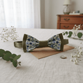 Mise en scène style mariage champêtre avec nœud papillon vert et fleuri posé près de branches d'eucalyptus et de fleurs de gypsophile.