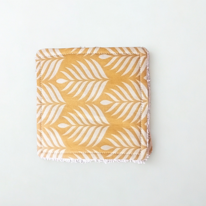 Vue de face d'une lingette lavable carrée au motif feuilles de palmes jaune moutarde. Gros plan sur le tissu coton imprimé.