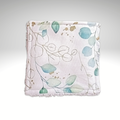 Gros plan sur le motif d'une lingette lavable : feuilles d'eucalyptus vert d'eau et touches dorées sur fond blanc.