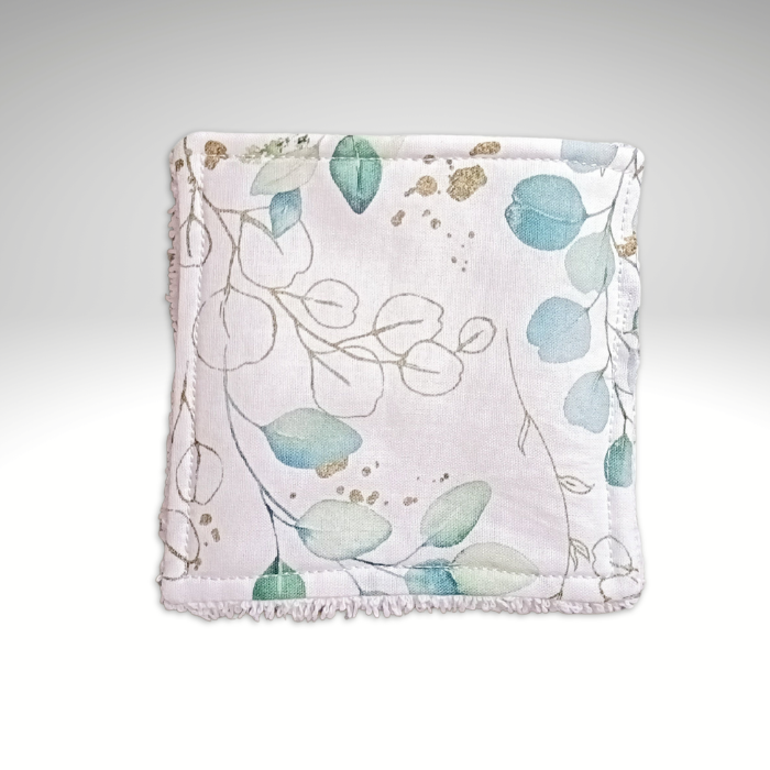 Gros plan sur le motif d'une lingette lavable : feuilles d'eucalyptus vert d'eau et touches dorées sur fond blanc.