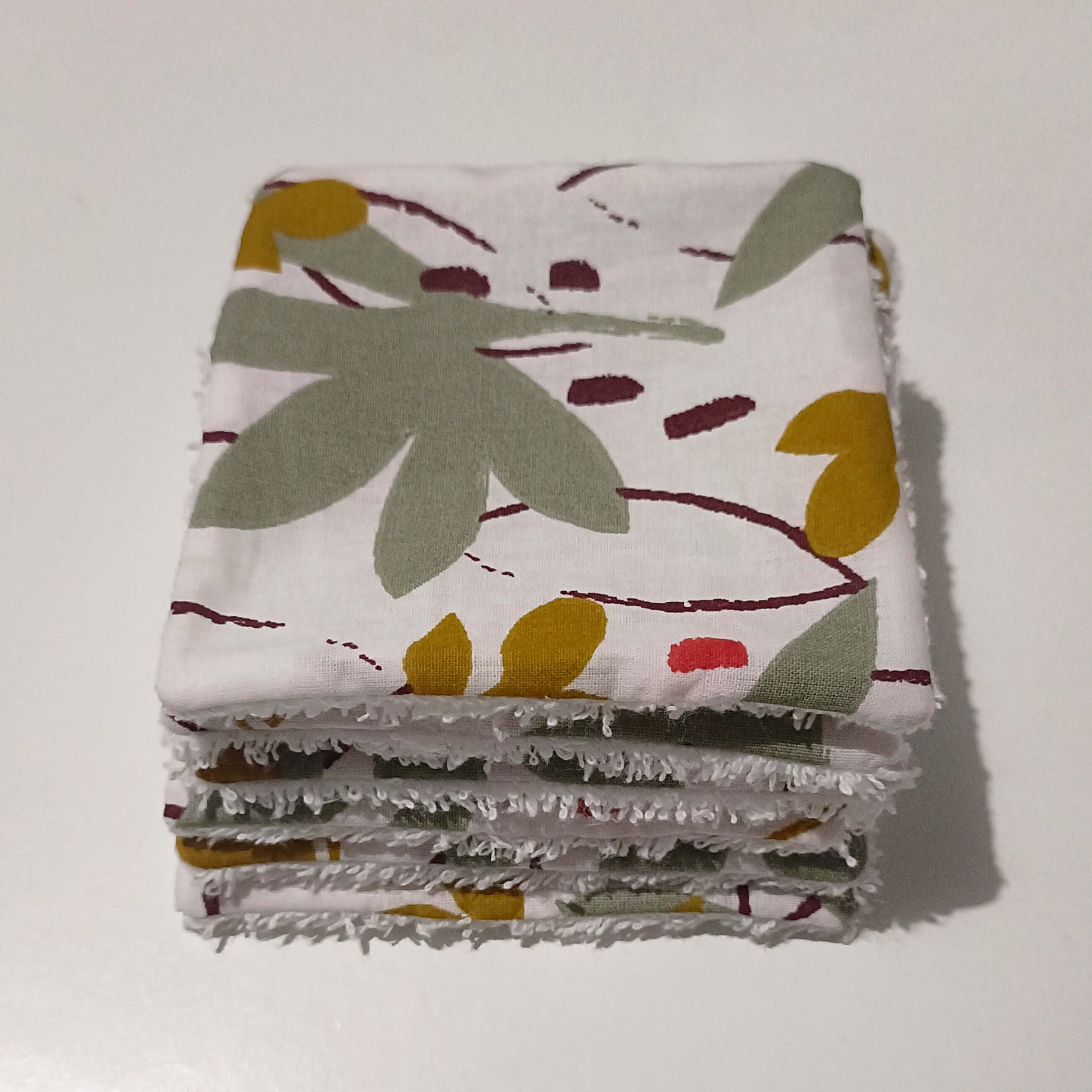 Pile de lingettes lavables bébé faites main, face motif floral sauge ocre et bordeaux, côté éponge blanc apparent sur les tranches