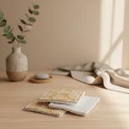 Mise en scène de lingettes lavables motif palmes moutarde et éponge bambou posées sur une table en bois. Ambiance décoration naturelle et zen avec vase.
