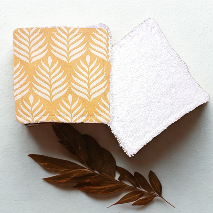 Vue recto-verso de deux lingettes lavables : une face en coton motif palmes jaune moutarde et une face en éponge de bambou blanche douce.