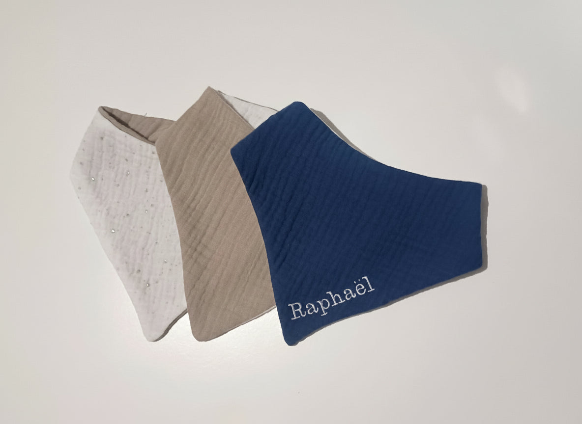 Trio de bavoirs bandana pour garçon en double gaze : bleu marine personnalisé Raphaël, beige sable et blanc à pois argentés.