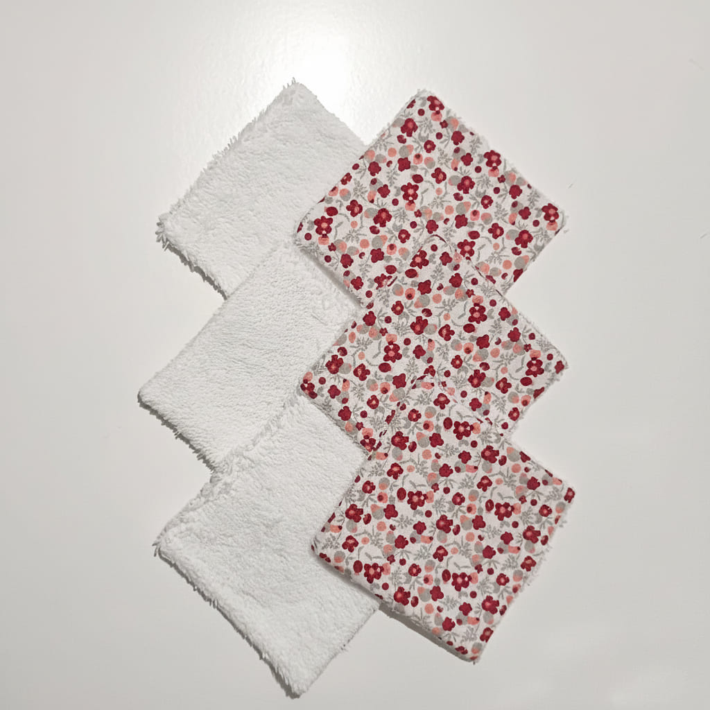 Disposition de 6 lingettes lavables alternant le côté tissu à fleurs rouges et le côté éponge blanche.