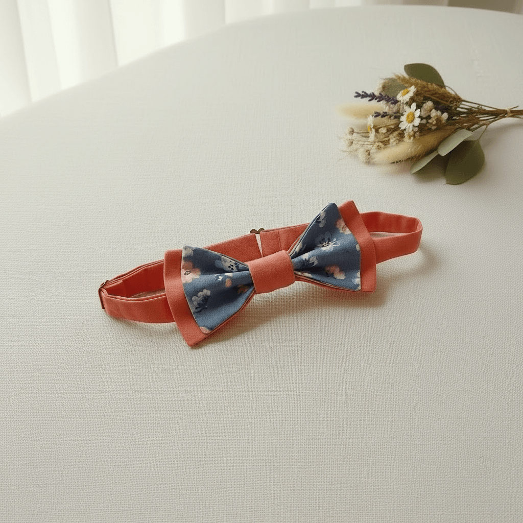Nœud papillon enfant réglable en terracotta et tissu bleu à fleurs délicates, posé sur table blanche avec bouquet de fleurs séchées, fait main L'Atelier de Megh