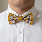 Homme portant un nœud papillon double jaune moutarde et motif floral liberty sur une chemise blanche pour une tenue de marié ou témoin.