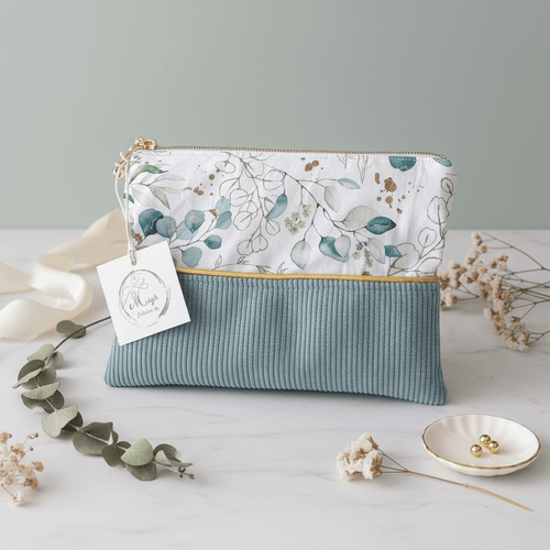 Petite pochette plate bi-matière associant un velours côtelé vert sauge et un imprimé aux délicates feuilles d'eucalyptus, souligné par un passepoil doré.