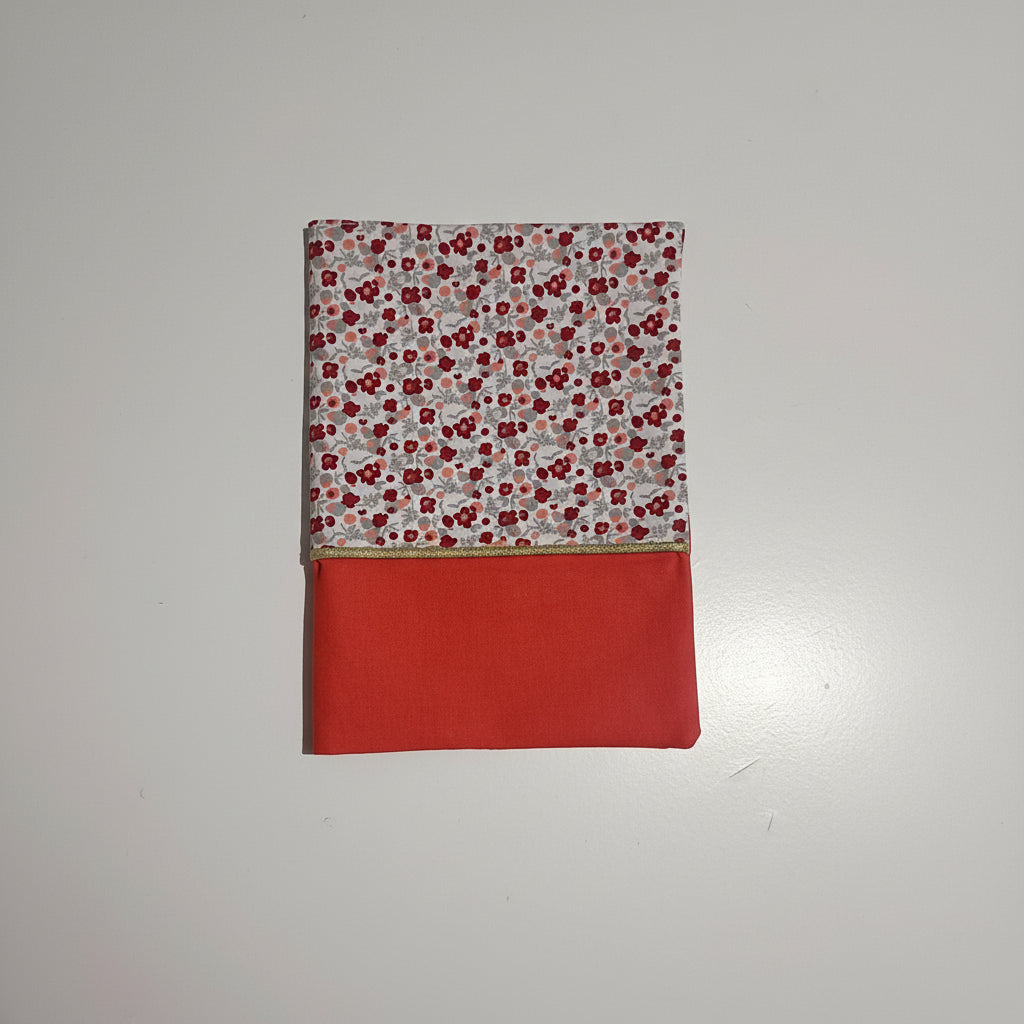 Vue de face d'un protège carnet de santé pour fille : tissu imprimé liberty à petites fleurs rouges et bas en coton uni couleur corail, séparés par un liseré doré.