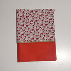 Vue de face d'un protège carnet de santé pour fille : tissu imprimé liberty à petites fleurs rouges et bas en coton uni couleur corail, séparés par un liseré doré.