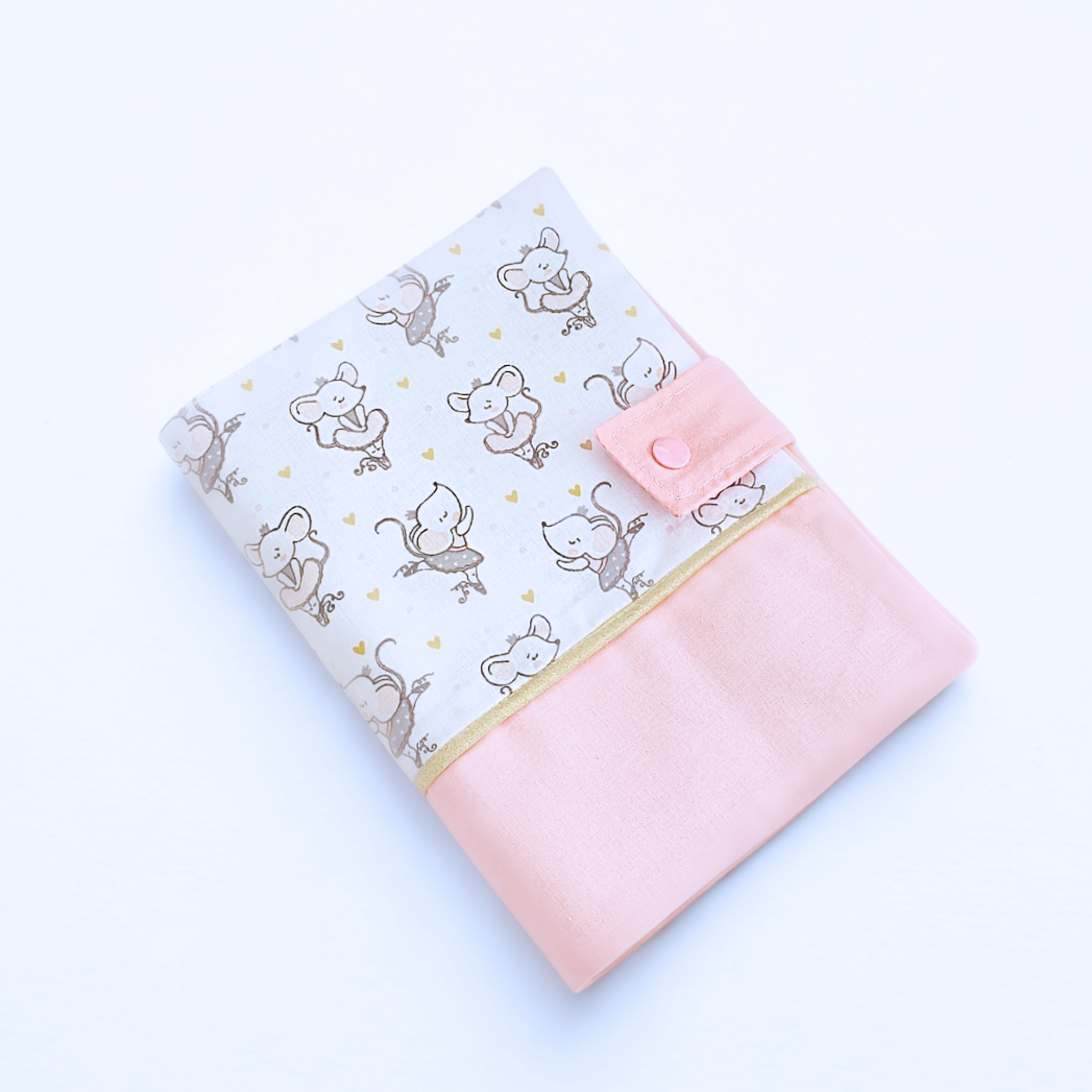 Vue de dessus du protège carnet de santé fermé, montrant l'association du tissu souris et du bas rose poudré avec le bouton pression assorti.
